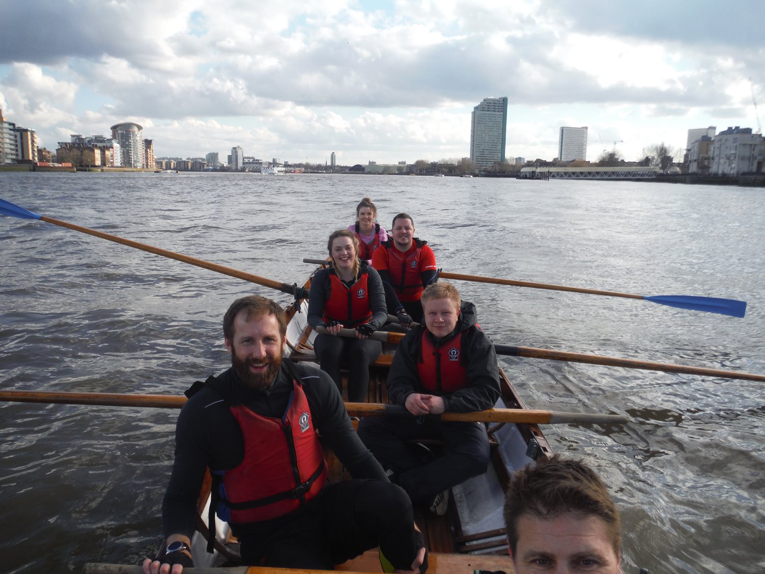 Team of employees volunteering in a charity rowing event, sitting in a rowing boat.