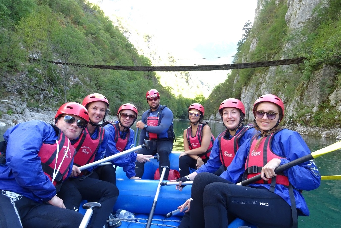 Employee volunteers in a white water raft wearing helmets and red life jackets.